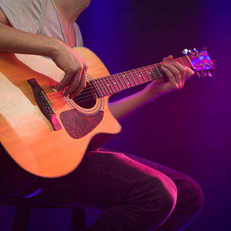 The musician plays an acoustic guitar. Beautiful background with colored light rays. The concept of music and playing a musical instrument.